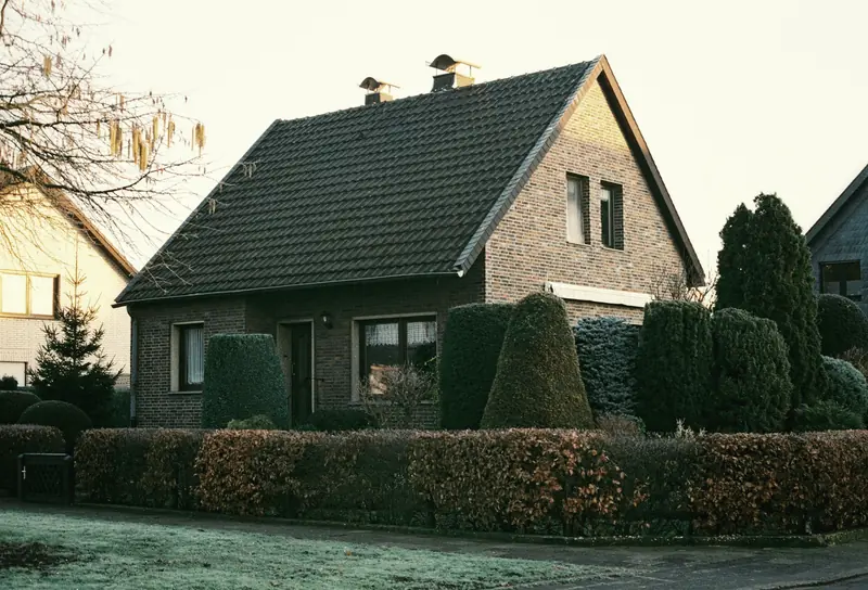 Einfamilienhaus mit Satteldach hinter einer geschnittenen Hecke (Symbolbild)