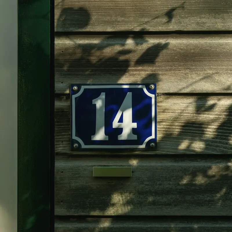 Blaue Emaille-Hausnummer 14 an einer Holzfassade