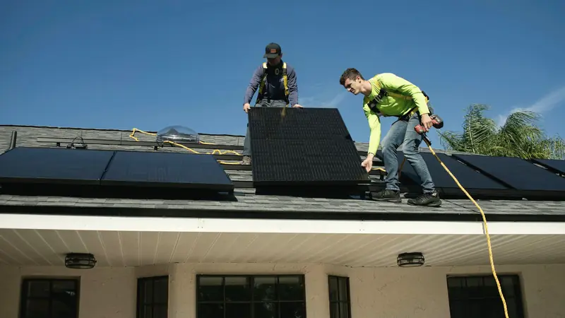 Zwei Monteure verlegen Solarmodule auf einem Hausdach
